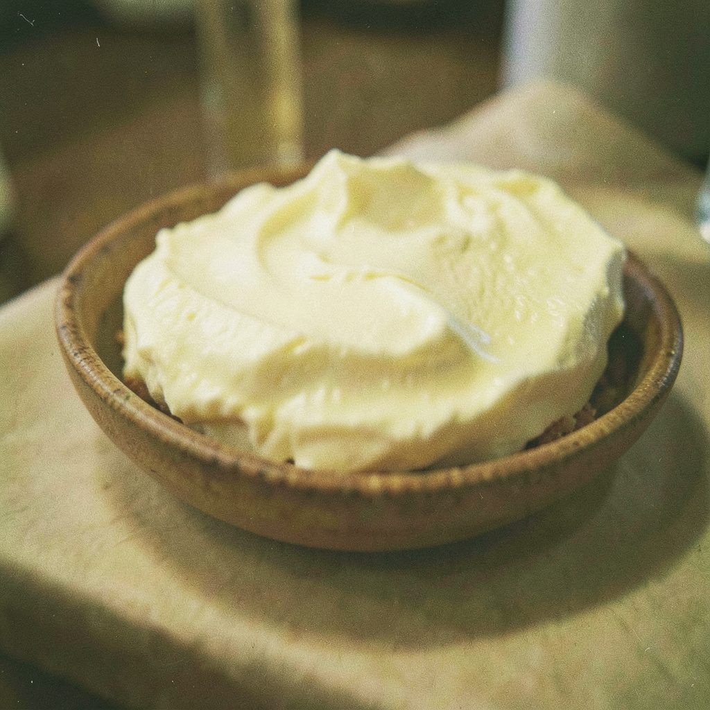 Analog film close-up of torn mozzarella and burrata on a wooden board, soft cream and sage-green tones, visible grain.