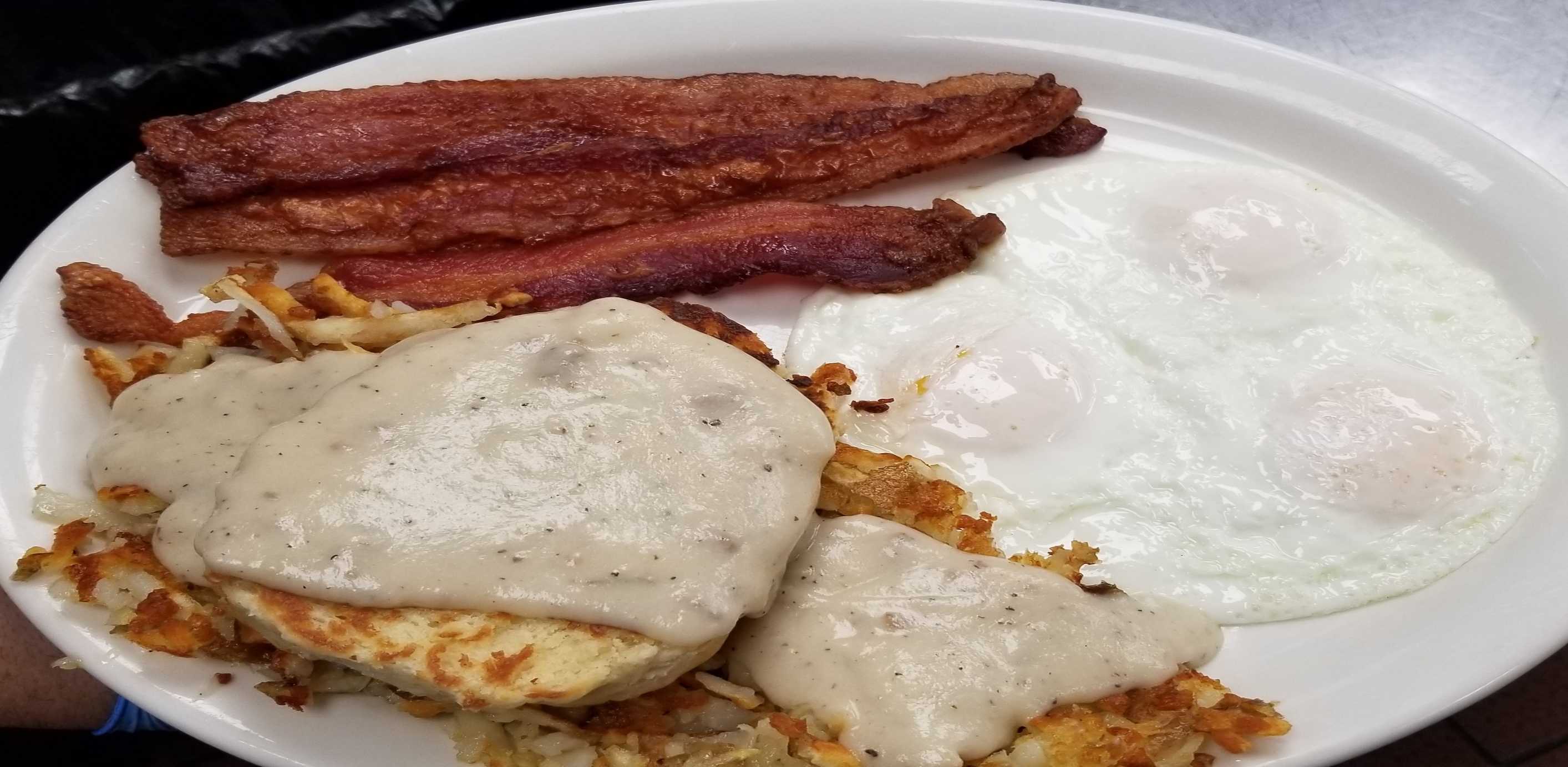 Analog film overhead of a diner plate with bacon, eggs, hash browns, and biscuits under gravy, mustard-yellow and crimson tones.