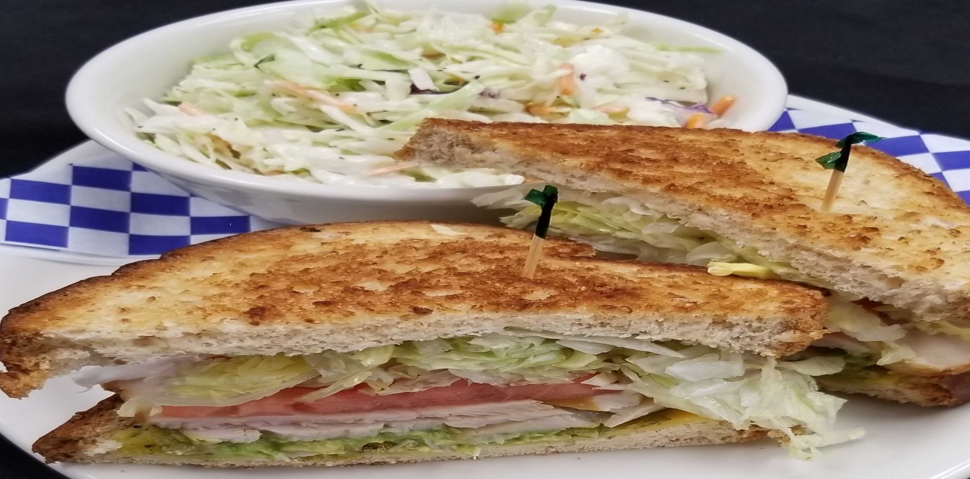 Analog film close-up of a toasted club sandwich cut in half with toothpicks beside a bowl of coleslaw, dusty mustard and warm beige tones.