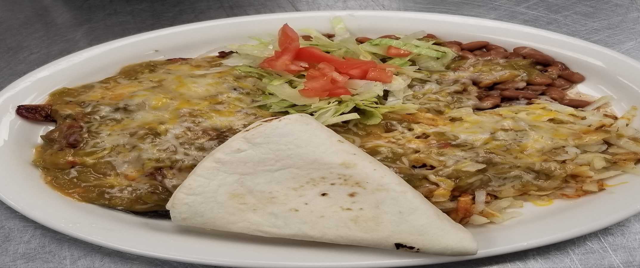 Analog film overhead of enchiladas in green sauce with beans and folded tortillas on an oval white plate, soft jade and terracotta tones.