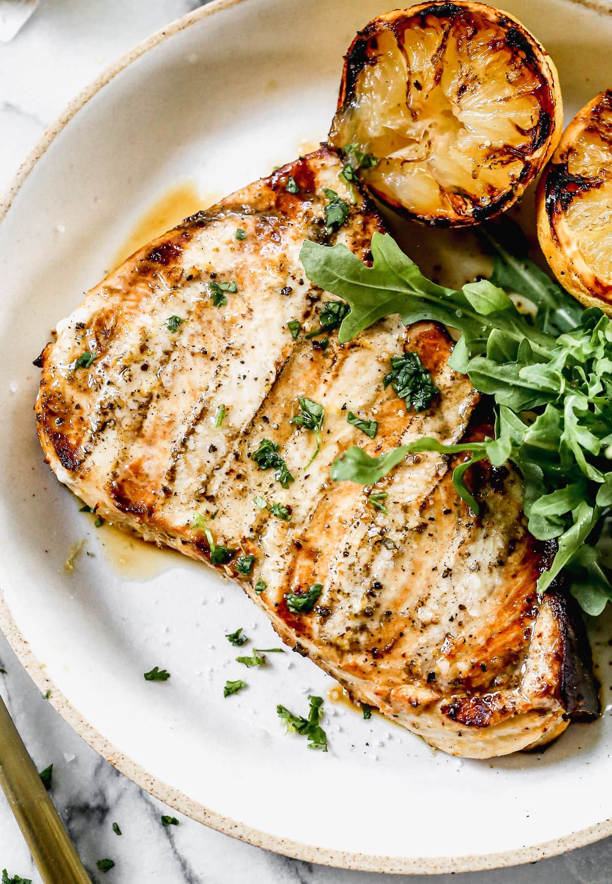 Analog film photograph with visible grain showing a grilled piece of meat topped with herbs, served with grilled citrus halves and fresh arugula on a warm-toned plate.